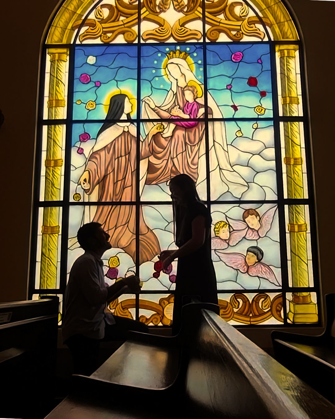 Aline e Arthur em silhueta diante de um vitral na igreja